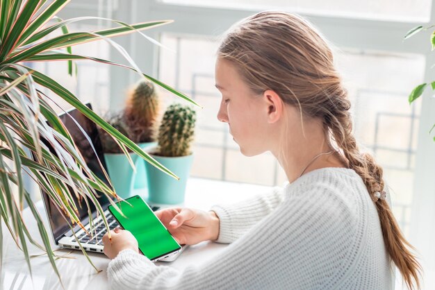 Beautiful young school girl working at home checking her phone with chromakey green screen