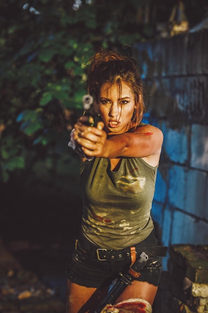 Красивая молодая серьезная женщина держит пистолет и готовится к нападению в заброшенных руинах.