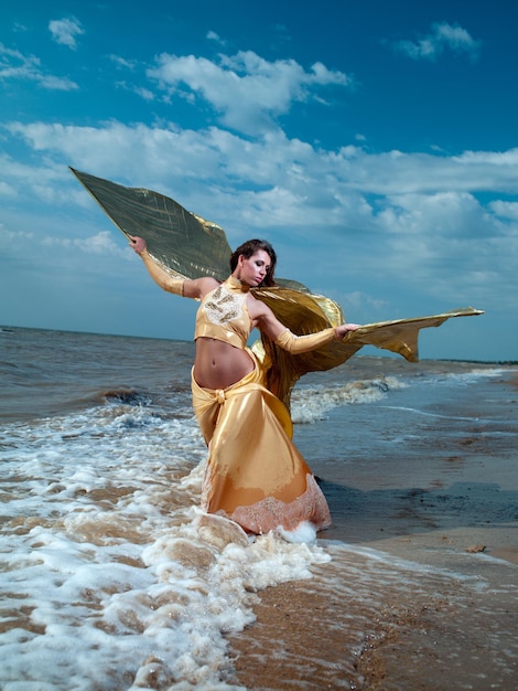 Beautiful young sexy fashion model in a chic gown on the beach