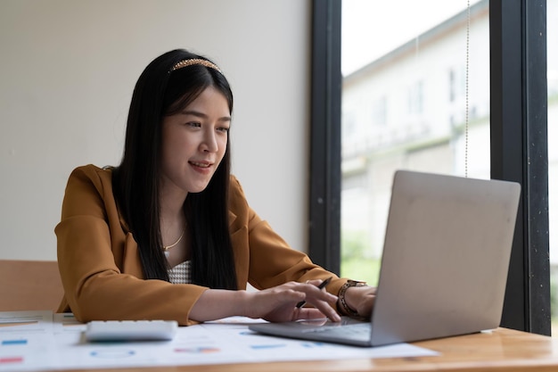 Beautiful young smiling Asian businesswoman working on laptop and drinking coffee Asia businesswoman working document finance and calculator in her office