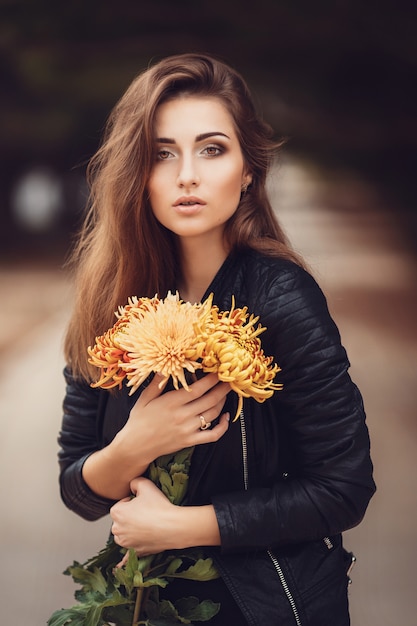 Beautiful young smiling brunette woman with flowers in autumn park