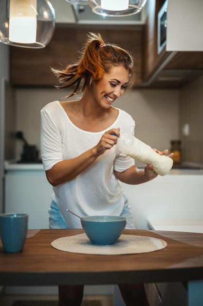 Foto bella giovane donna allegra sorridente sta preparando la sua sana colazione nella sua cucina, divertendosi e ballando.