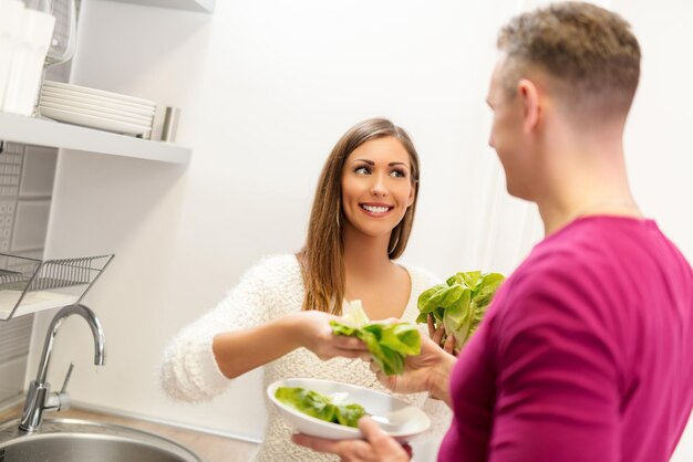 Beautiful young smiling couple preparing lettuce in the kitchen.