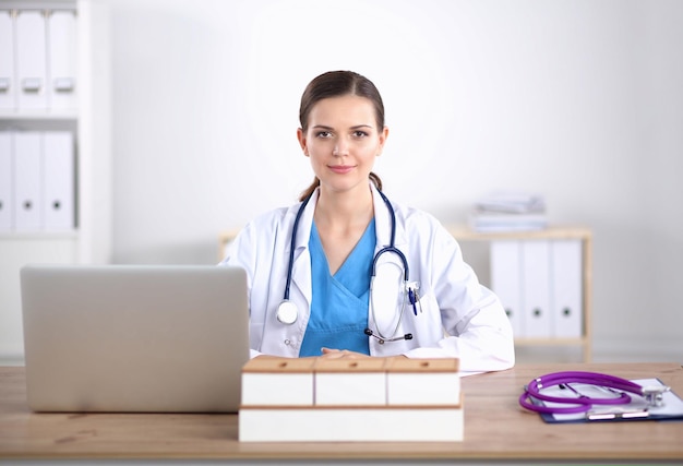 Beautiful young smiling female doctor sitting at the desk and writing female doctor