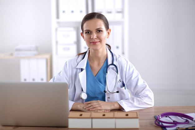 Beautiful young smiling female doctor sitting at the desk and writing