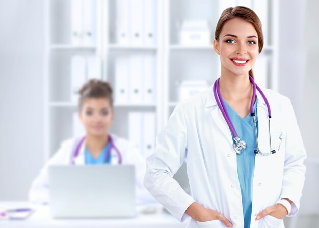 Beautiful young smiling female doctor sitting at the desk and\
writing