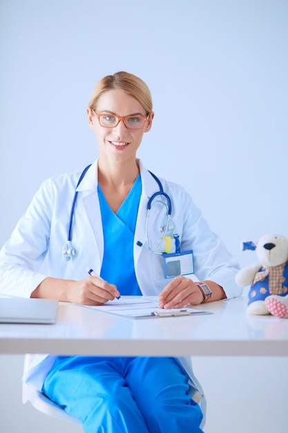 Bello giovane medico femminile sorridente che si siede allo scrittorio.