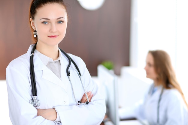 Beautiful young smiling female doctor standing in a hospital with her colleague in the background.