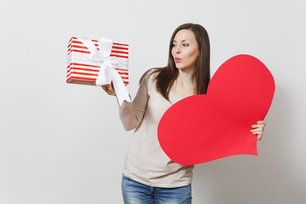Beautiful young smiling woman holding big red heart, box with present on white background. Copy space for advertisement. With place for text. St. Valentine's Day or International Women's Day concept.