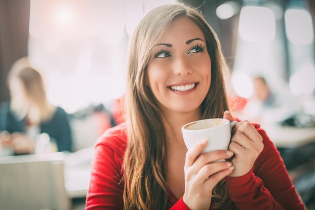 リラックスしてカフェでコーヒーを楽しんでいる美しい若い笑顔の女性。