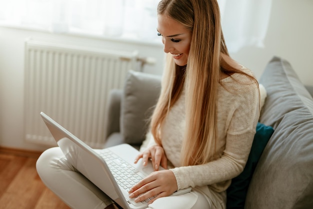 Beautiful young smiling woman relaxing at the home and surfing the net on a laptop.