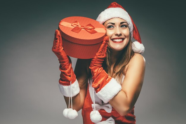 赤いプレゼントを持って楽しんでいるサンタクロースの衣装で美しい若い笑顔の女性。