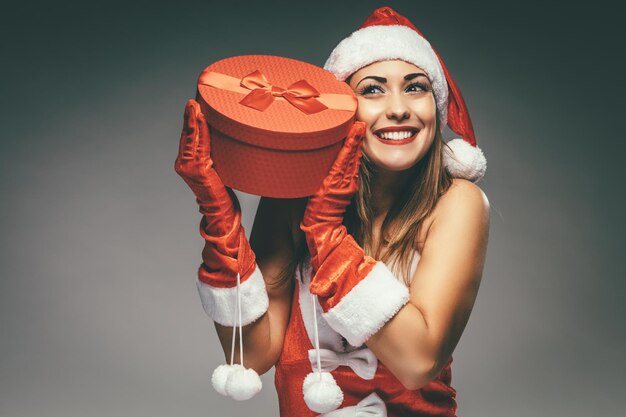 Photo beautiful young smiling woman in santa claus costume holding red present and having fun.