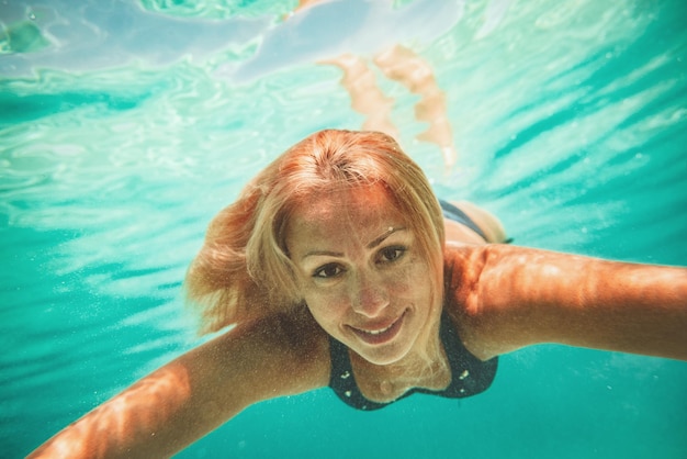 Beautiful young smiling woman swimming underwater in the sea.