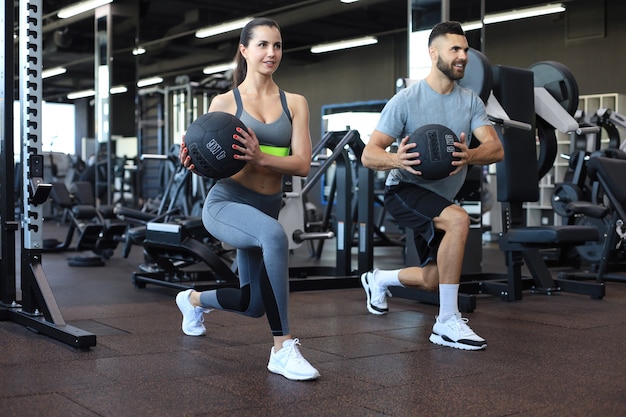 Beautiful young sports couple is working out with medicine ball in gym.