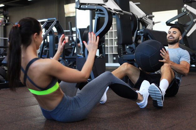 Beautiful young sports couple is working out with medicine ball in gym.