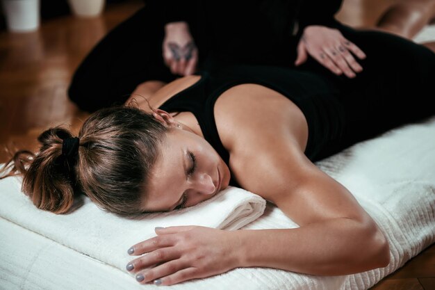 Foto bella giovane donna sportiva che si gode un massaggio alla schiena shiatsu sdraiata sul pavimento di legno con una maglietta nera