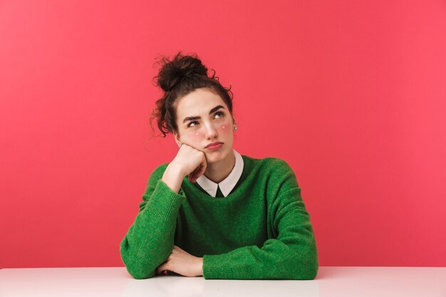 Beautiful young student girl sitting at the table isolated, looking away