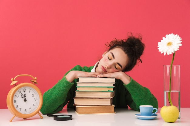 Beautiful young student girl sitting at the table isolated, studying with books, sleeping