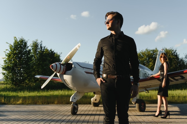 Beautiful young stylish couple in official clothes standing near private plane