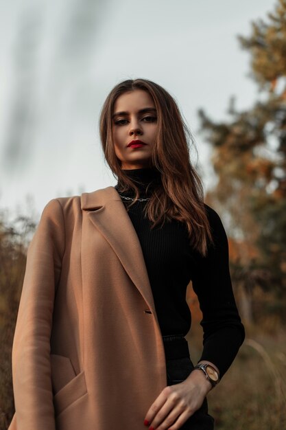 Beautiful young stylish woman in a fashionable coat with a vintage sweater outdoors in a field with grass