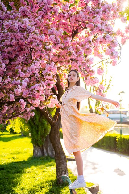 さくら公園を歩いて、咲くピンクの花の美しさを楽しむ美しい若いスタイリッシュな女性