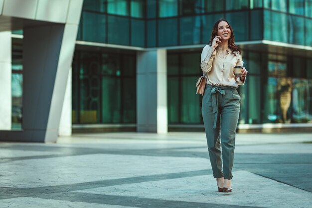 Beautiful young successful woman is talking on a smartphone\
against urban city background.