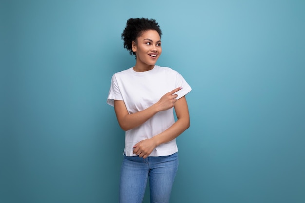 Beautiful young swarthy woman with fluffy curly hair dressed in a white tshirt points her hand to