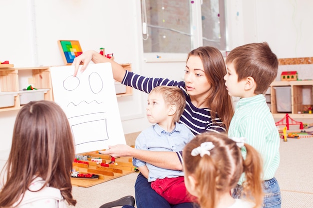 Beautiful young teacher showing figures preschoolers, children sit in a circle