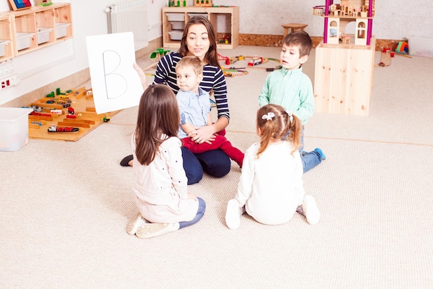 Beautiful young teacher showing letter preschoolers, children sit in a circle