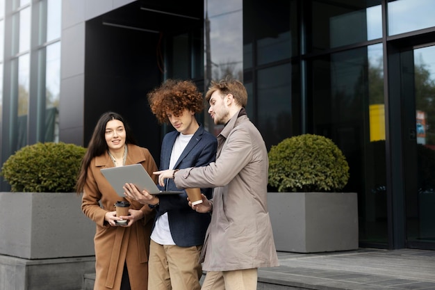 Bella giovane squadra di lavoratori che lavorano all'aperto utilizzando il computer portatile i giovani si avvicinano all'ufficio moderno