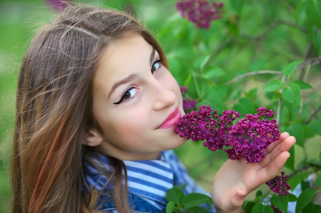 Beautiful young teen girl standing in the flowers of lilac.