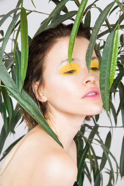 Beautiful young teen girl with perfect skin with fresh yellow color makeup and green plant. Natural beauty woman. Skincare face care beauty salon spa treatment concept