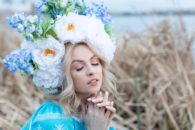 아름다운 꽃 화환과 함께 파란색 수 놓은 드레스를 입은 아름다운 젊은 우크라이나 여성