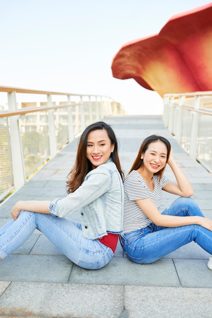 写真 橋の上に背中合わせに座って、カメラに微笑んで美しい若いベトナムの女性の友人