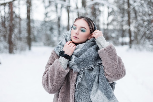 雪に覆われた森の中でスカーフと毛皮のコートと冬の古着の美しい若い流行の女の子モデル。屋外のロシアの女の子