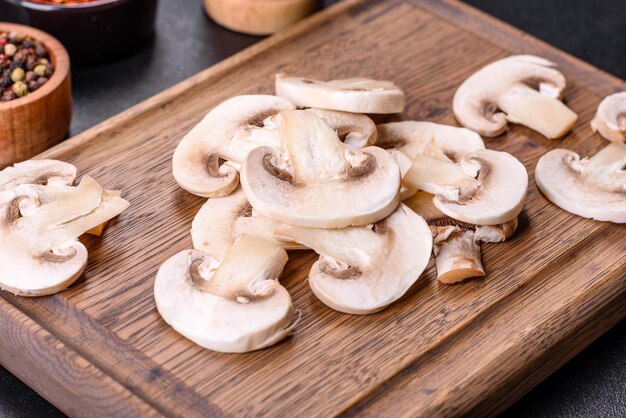 Beautiful young white champignons torn to slices on a dark concrete background