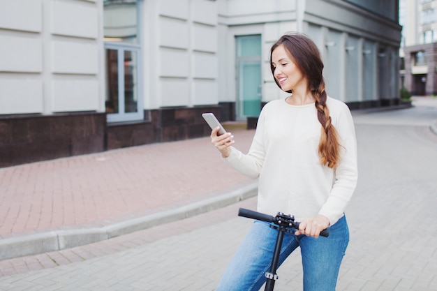 Beautiful, young, and white-toothed girl with long brown hair stopped while riding the scooter