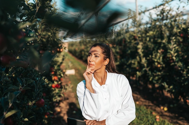 Красивая молодая женщина-агроном работает в яблоневом саду.