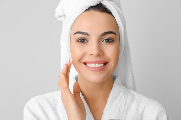 Beautiful young woman applying cream against grey background