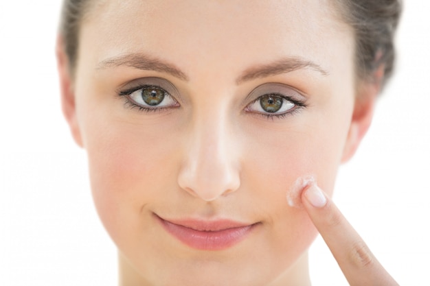 Beautiful young woman applying cream to her face