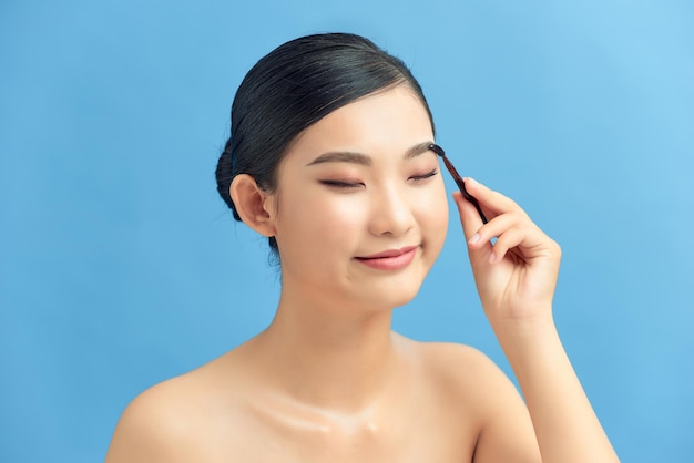 Beautiful young woman applying eyebrow brush on blue