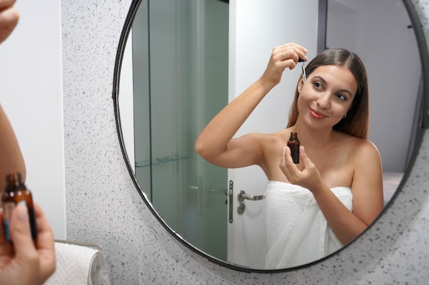 Beautiful young woman applying hyaluronic acid with pipette in bathroom