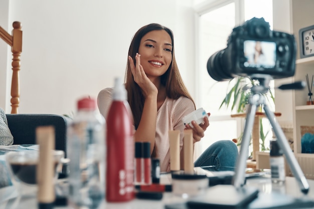 Beautiful young woman applying lip gloss and smiling while making social media video