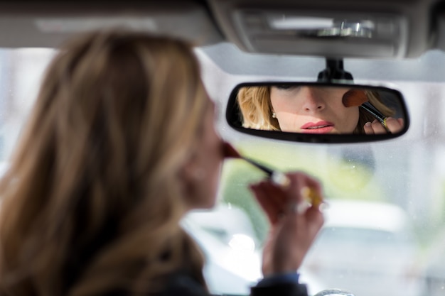 Foto bella giovane donna che stende il trucco mentre guidando automobile