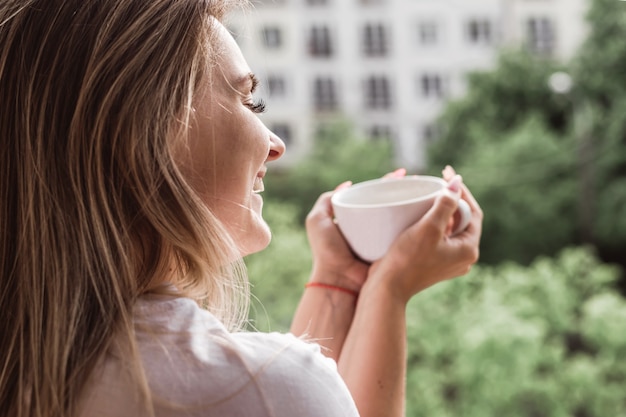 お茶と朝を楽しむバルコニーで美しい若い女性