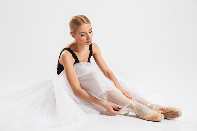 Beautiful young woman ballerina sitting on floor