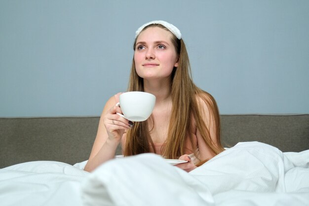 Beautiful young woman in bed with cup of tea