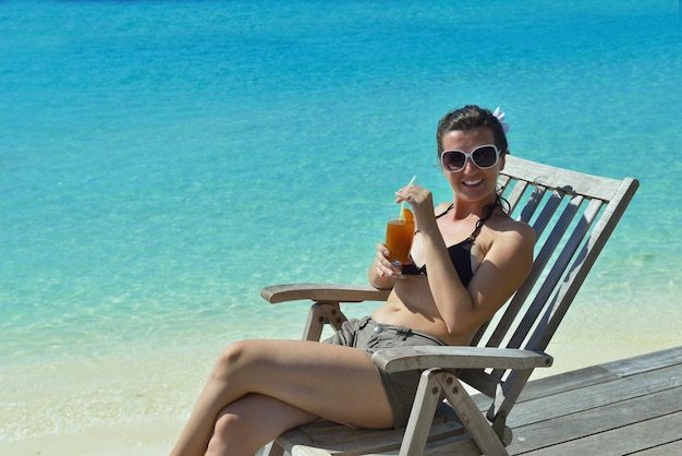 Beautiful young woman in bikini lying on a deckchair with a drink by the sea