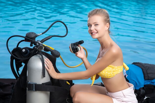 A beautiful young woman in a bikini sits near diving equipment